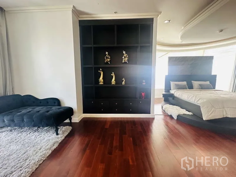 Condominium for rent or sale in Khlong Toei, Bangkok - Master suite lounge with display shelving, chaise and raised bed platform on polished wood floors.