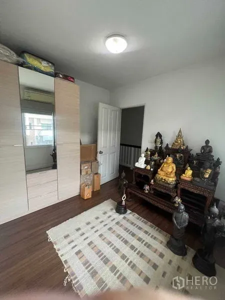 Townhouse for rent in Bueng Kum, Bangkok - Compact upstairs room with wardrobe, rug and display shelves.