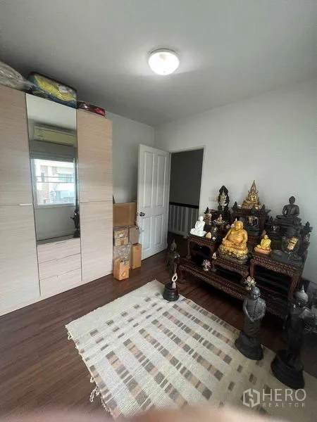 Townhouse for rent in Bueng Kum, Bangkok - Compact upstairs room with wardrobe, rug and display shelves.