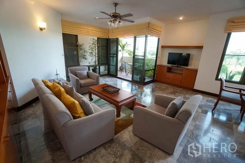 Apartment for rent in Watthana, Bangkok - Cozy lounge with sofa set, ceiling fan and sliding doors opening to a green balcony.