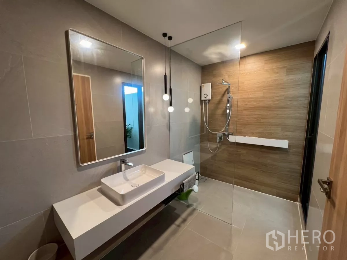 Detached House for rent in Samut Prakan - Modern bathroom with floating vanity and glass shower, wood-tone wall.
