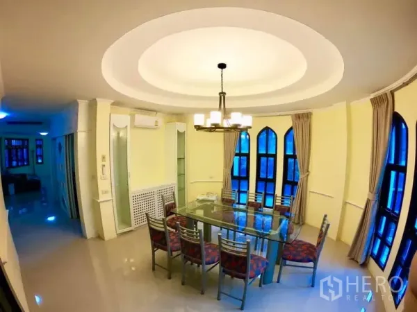 联排别墅 出租在Watthana, Bangkok - 采光明亮的餐厅，玻璃餐桌八把椅子，吊灯与拱形窗。