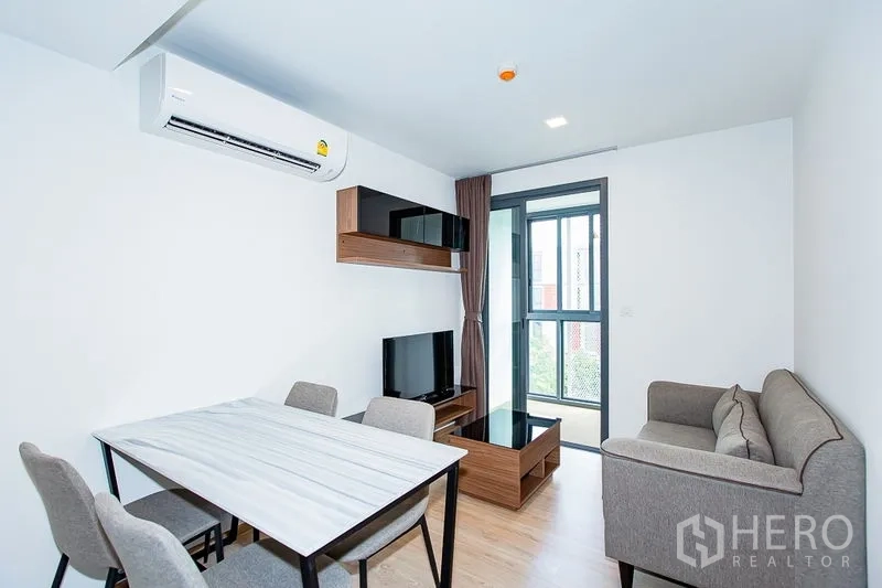 公寓 出租在Watthana, Bangkok - 客厅设壁挂层架与电视柜，通往阳台，配餐桌椅。