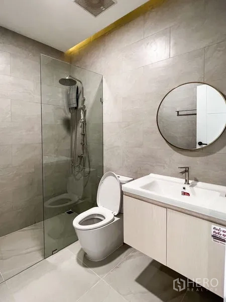 Townhouse for rent or sale - Light-toned bathroom with round mirror, glass shower and built-in vanity.