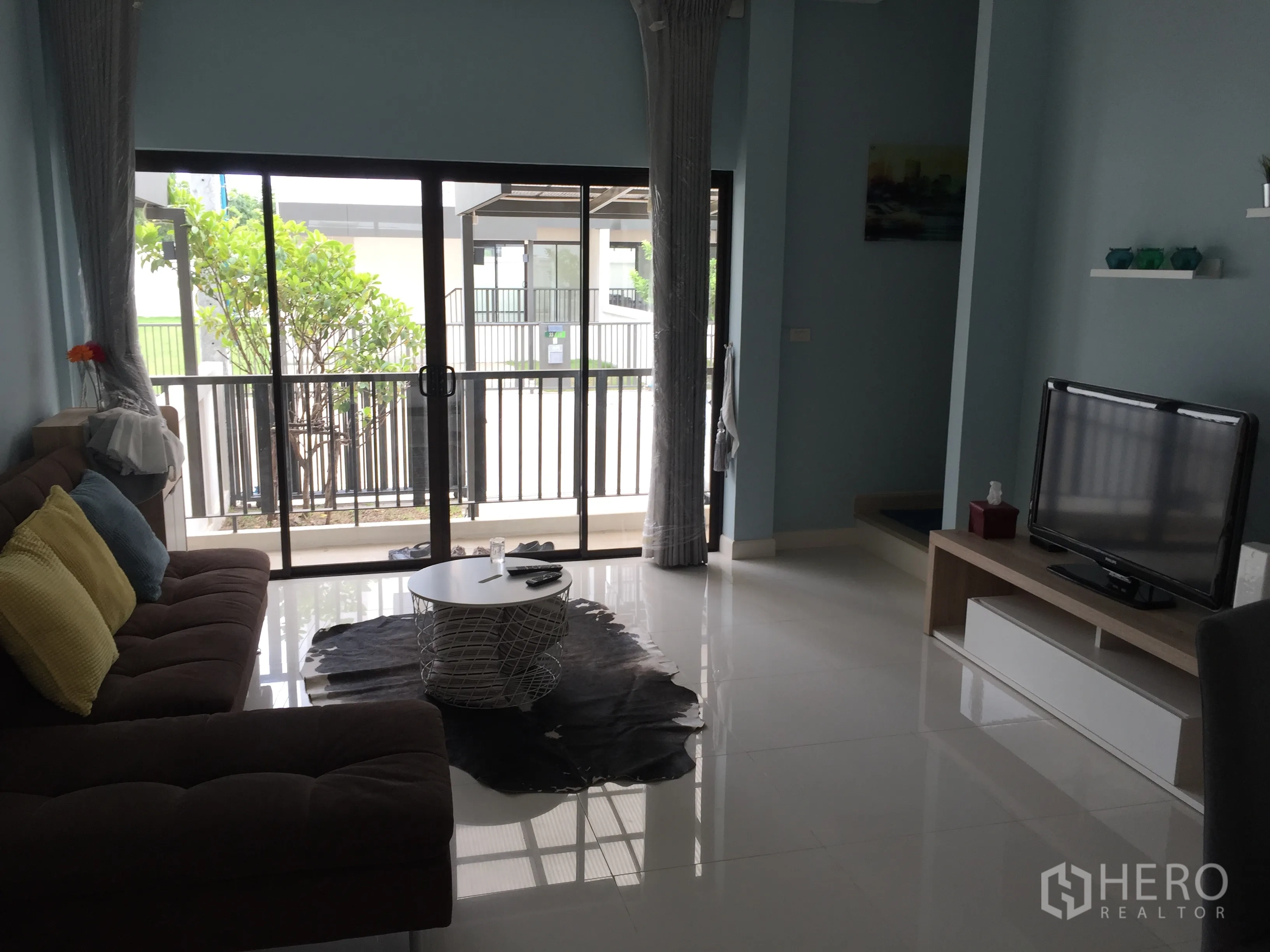 Townhouse for rent in Saphan Sung, Bangkok - Living room facing full-height sliding doors to balcony, glossy tile flooring and TV cabinet.
