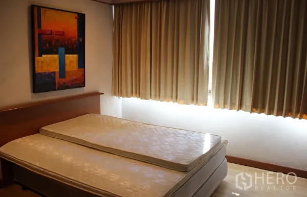 Condominium for rent in Khlong Toei, Bangkok - Second bedroom with a mattress, large curtained windows, and warm wood flooring.