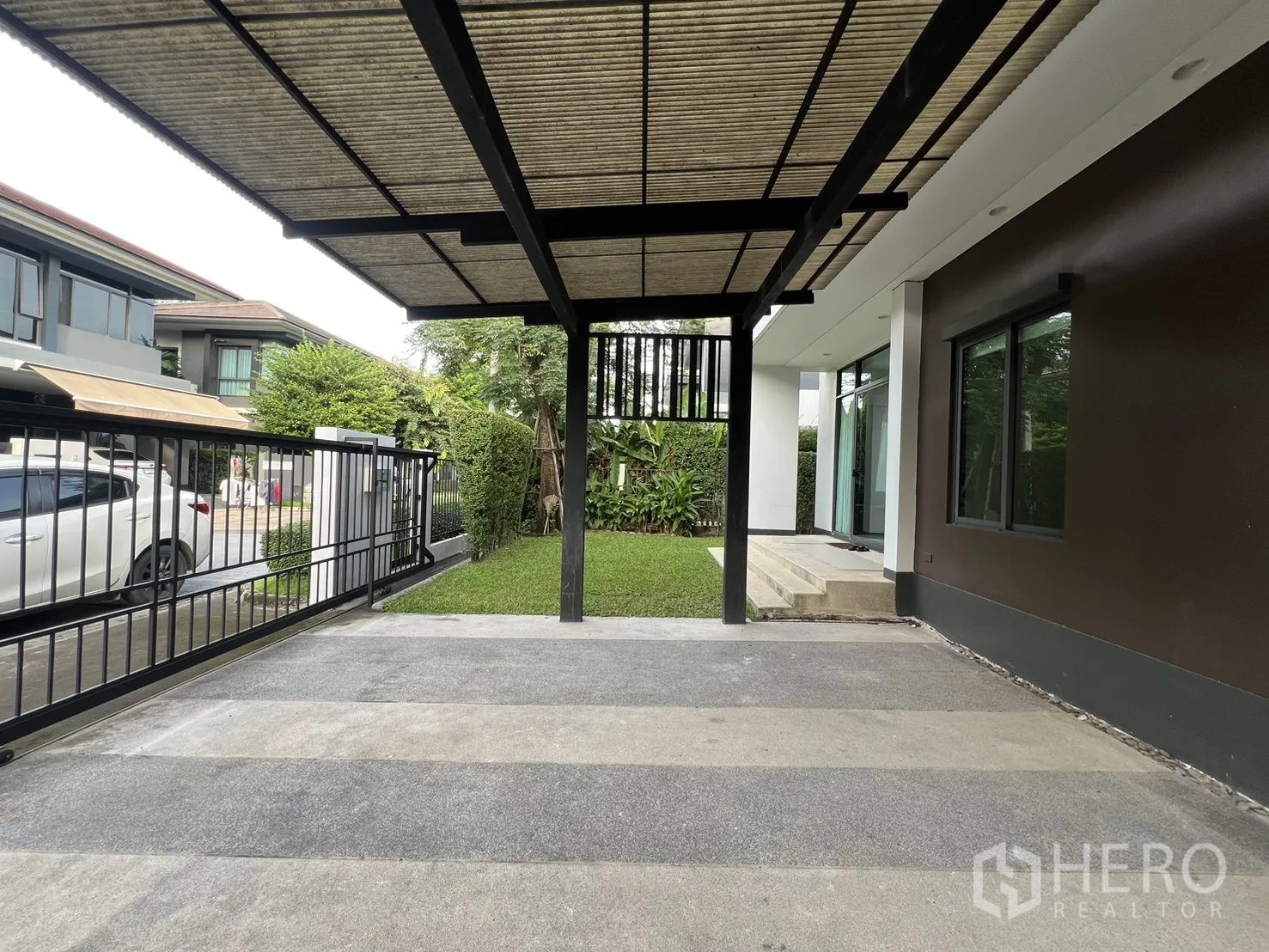 Detached House for rent in Bang Kapi, Bangkok - View from the carport toward the street with the gate and a small garden.