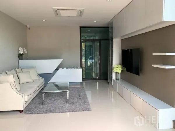 Home Office for rent - Reception-style lounge with sofa, glass coffee table and media wall facing a glass entry door.