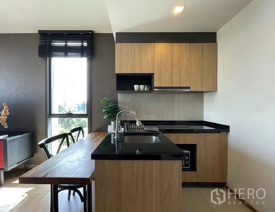 Condominium for rent in Watthana, Bangkok - L-shaped kitchen with black countertops and a window bringing natural light.