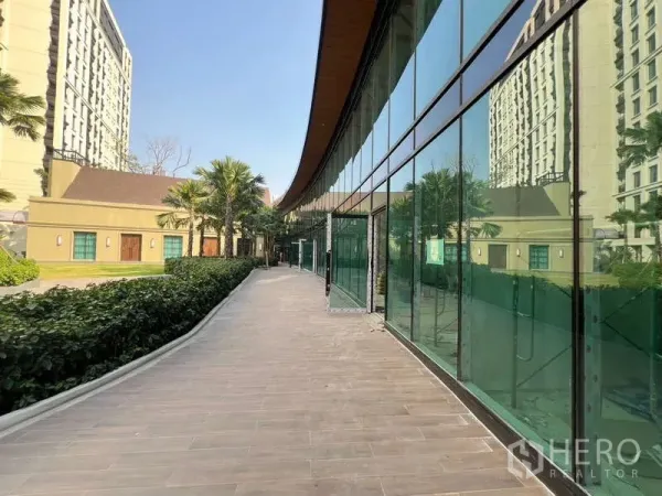Retail Space for rent in Watthana, Bangkok - Landscaped path with hedges and palm trees beside green-tinted storefronts.