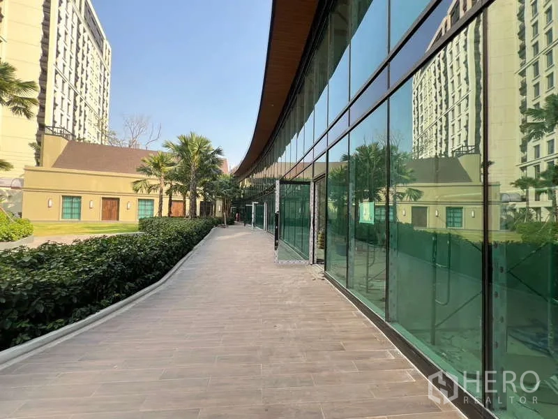 Retail Space for rent in Watthana, Bangkok - Landscaped path with hedges and palm trees beside green-tinted storefronts.