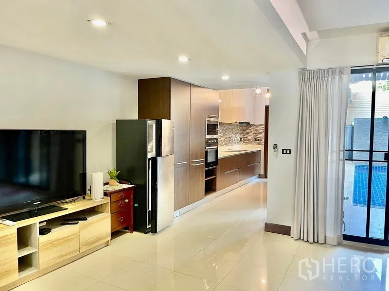 联排别墅 出租在Khlong Toei, Bangkok - 开放式起居区与内置厨房，现代电器，玻璃门通往泳池。