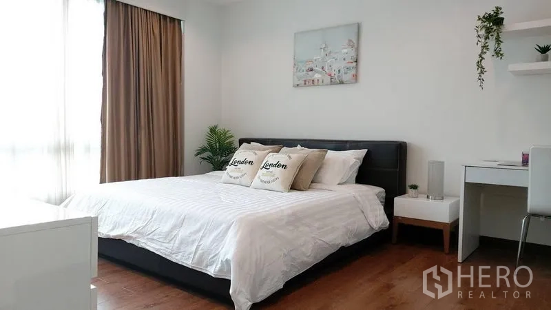 Condominium for rent in Phra Khanong, Bangkok - Airy bedroom with large bed, white linens, study desk, side tables, wall art and natural light from big windows.