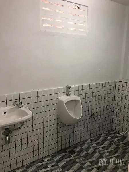 Warehouse for rent in Khlong Luang, Pathum Thani - Tiled restroom with a wall-mounted sink and urinal inside the warehouse.