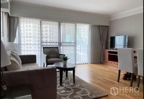 Condominium for rent in Sathon, Bangkok - Sunlit Sathon condo living room with sofa, armchair, coffee table and floor-to-ceiling windows.