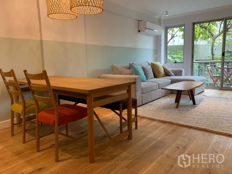 Condominium for sale in Watthana, Bangkok - Bright living and dining area with wood floors, sofa and balcony overlooking greenery.