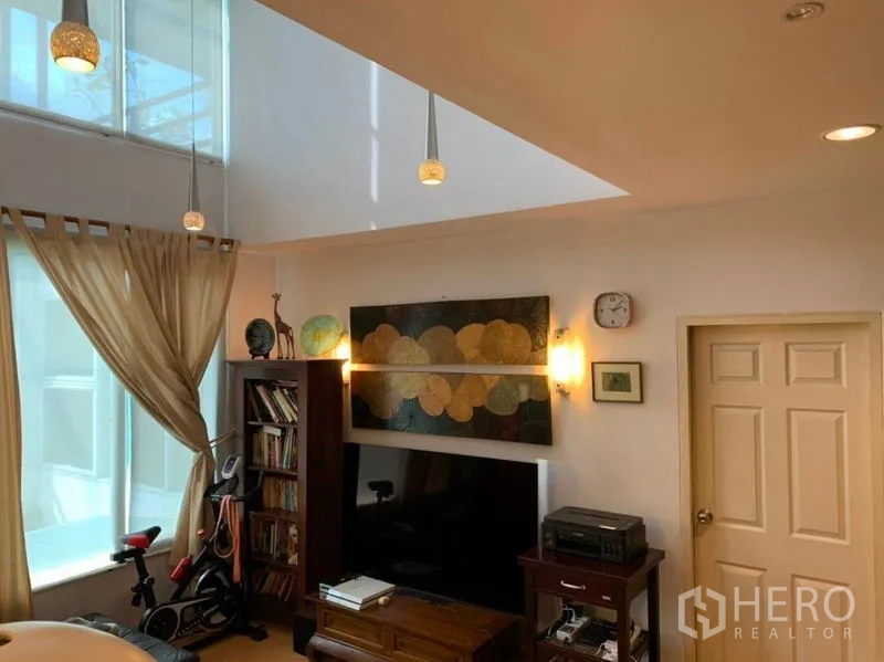 Detached House for sale in Suan Luang, Bangkok - Family room under a skylight with TV wall, bookshelves and an exercise bike.