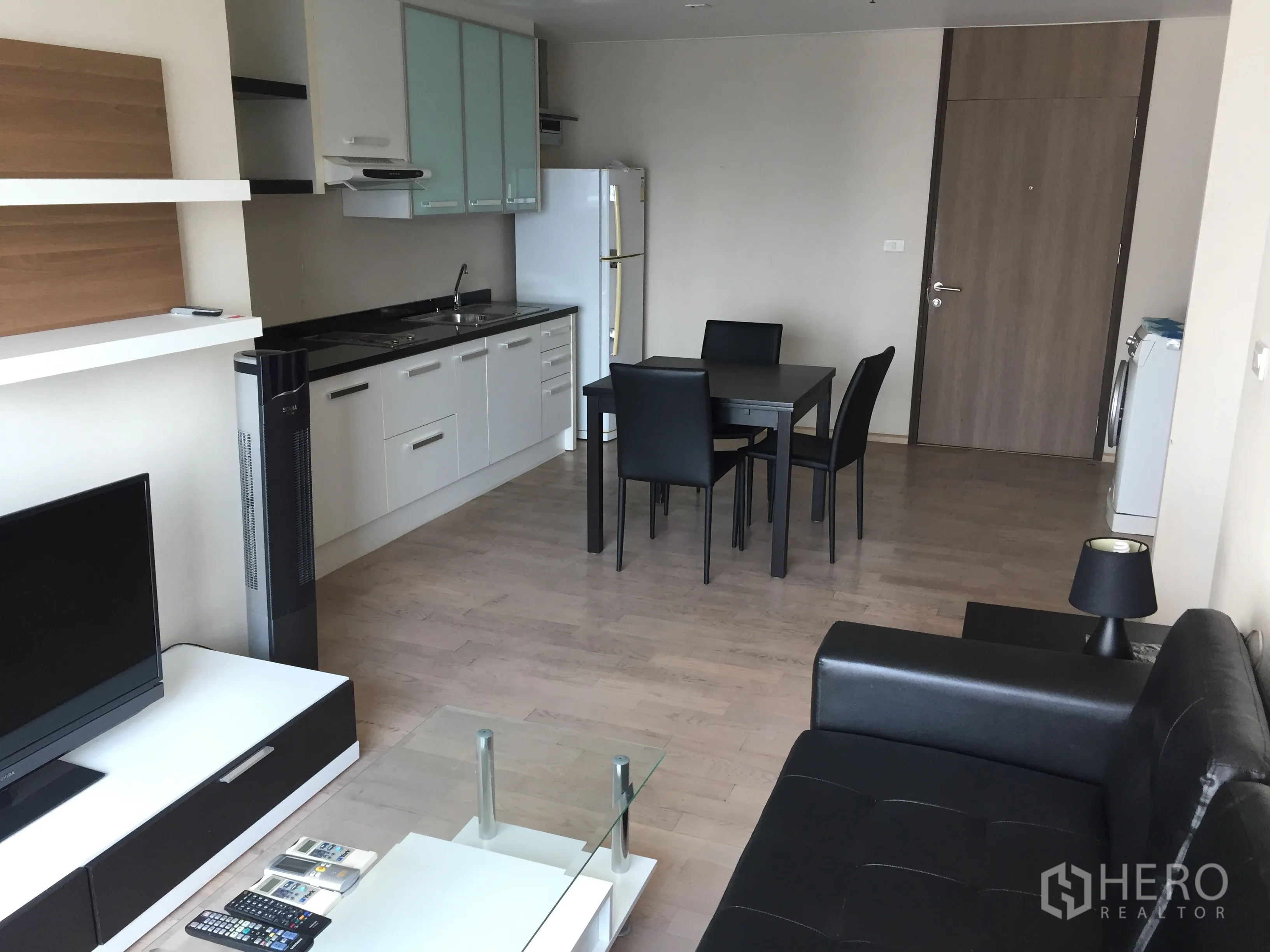 Condominium for rent in Khlong Toei, Bangkok - Open-plan living and kitchen with sofa, TV unit and dining set on light wood floors.