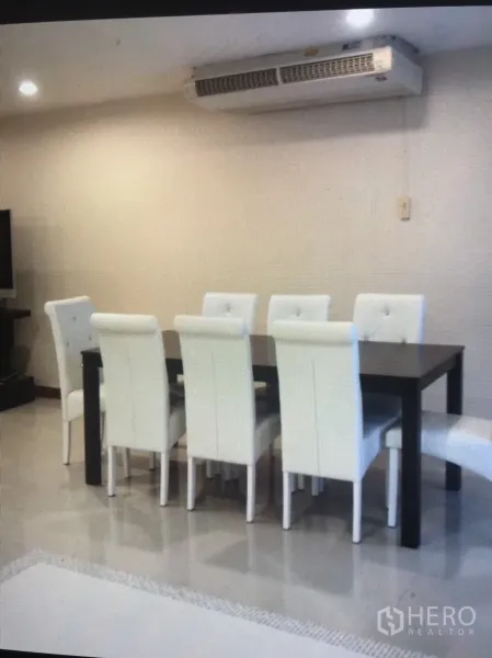 Condominium for rent in Bang Rak, Bangkok - Dining area with a dark table and six white tufted chairs beneath a wall-mounted air conditioner.
