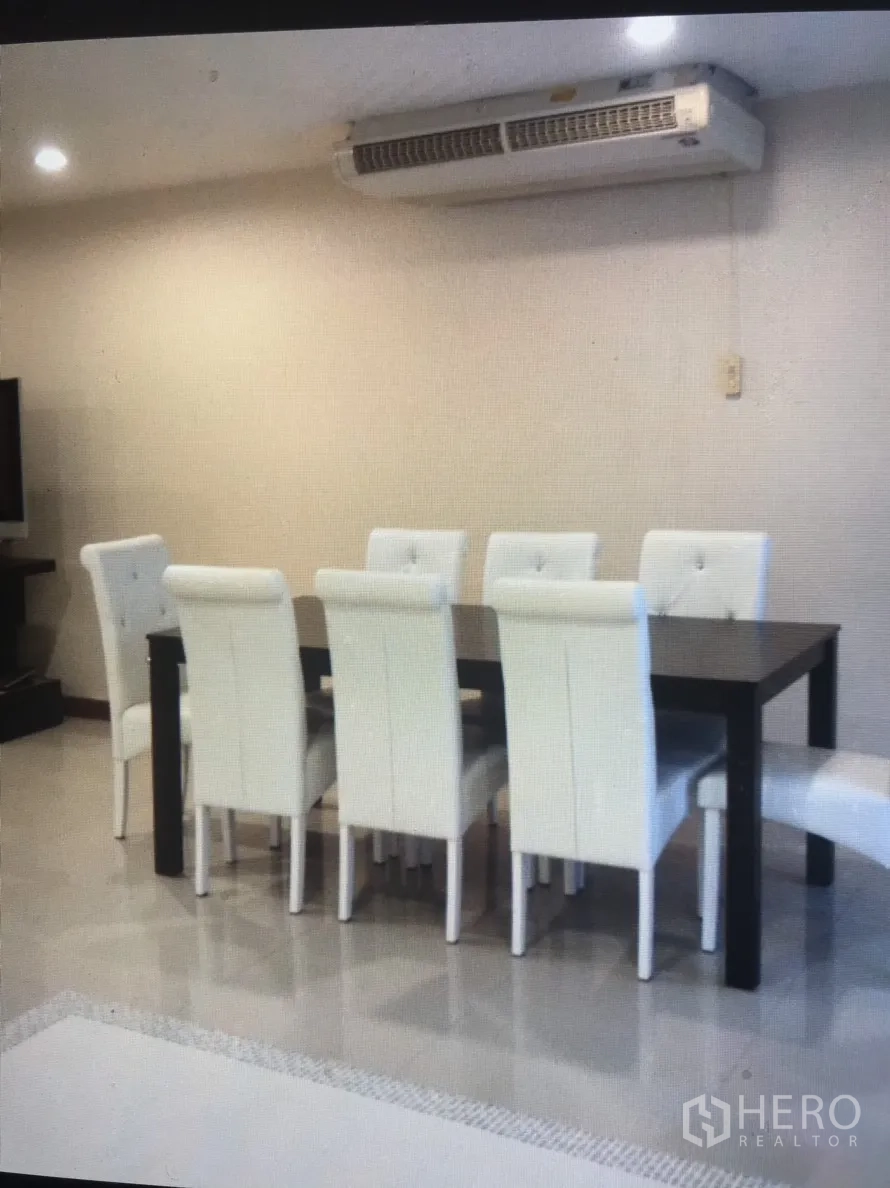 Condominium for rent in Bang Rak, Bangkok - Dining area with a dark table and six white tufted chairs beneath a wall-mounted air conditioner.