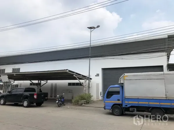 Factory for rent in Nonthaburi - Angled exterior of the warehouse showing a covered carport and gray roller door with a streetlight.