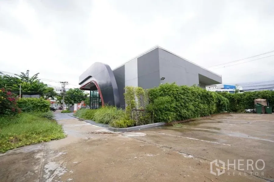 Standalone for rent in Bang Na, Bangkok - Rear angle of grey standalone building with parking apron and hedges.