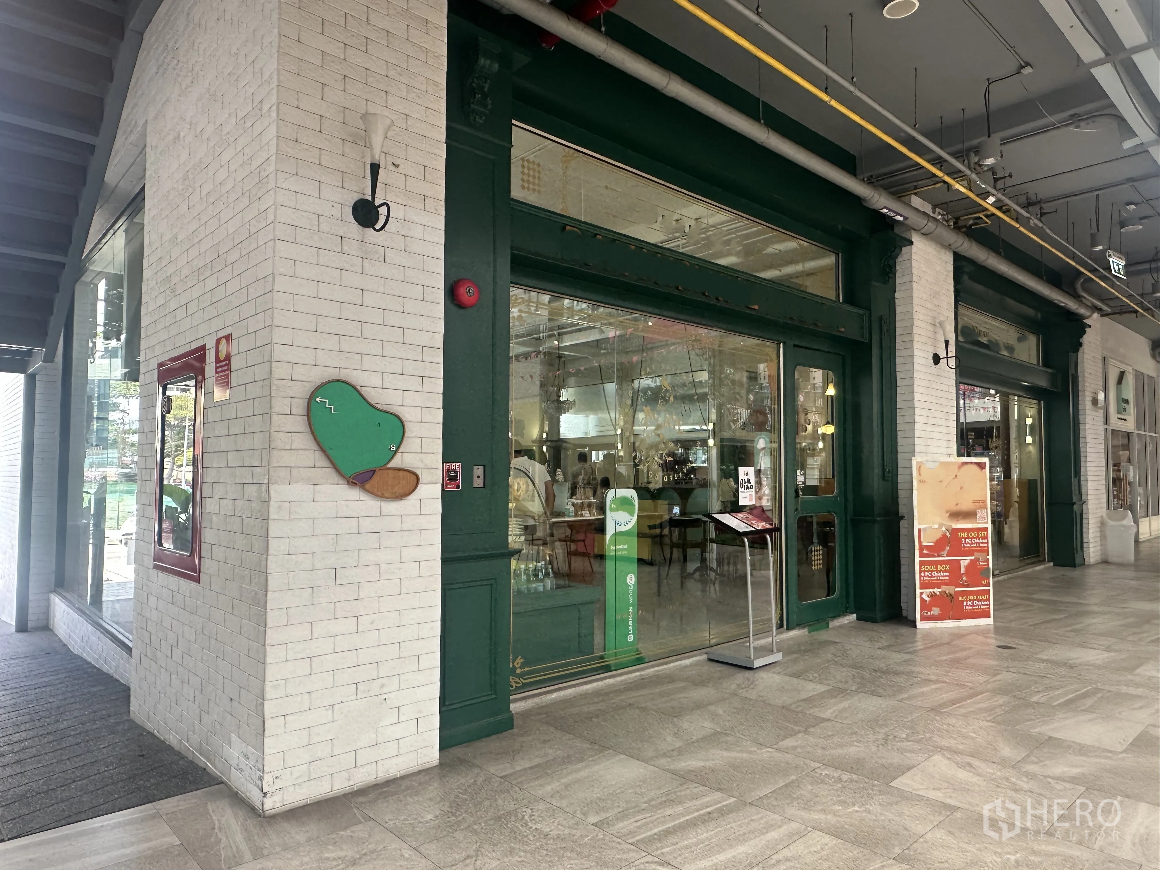 零售空间 for sale in Khlong Toei, Bangkok - 沿有顶走道的宽店面外立面，玻璃门与招牌位，外露管线的高天花和瓷砖地面。