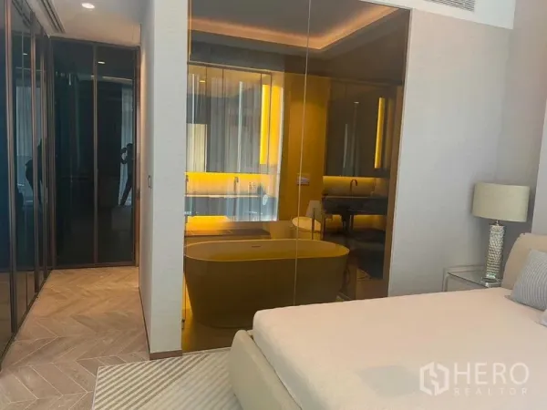 Condominium for rent in Khlong Toei, Bangkok - Bedroom with glass wall to a bathroom featuring a freestanding tub and warm lighting.