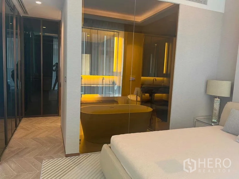Condominium for rent in Khlong Toei, Bangkok - Bedroom with glass wall to a bathroom featuring a freestanding tub and warm lighting.
