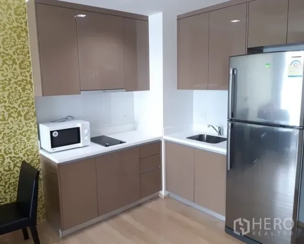 Condominium for rent in Khlong Toei, Bangkok - Compact corner kitchen with glossy cabinets, cooktop, microwave and stainless refrigerator.