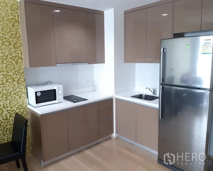 Condominium for rent in Khlong Toei, Bangkok - Compact corner kitchen with glossy cabinets, cooktop, microwave and stainless refrigerator.