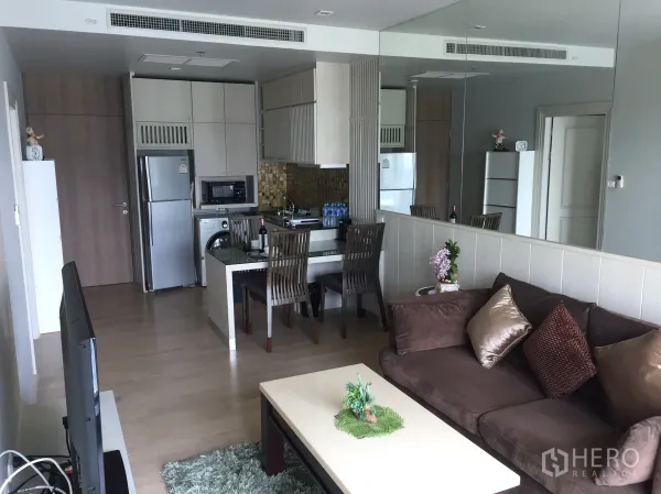公寓 出租在Bangkok - 开放式客厅带镜面墙，沙发、电视与餐区相连的小巧厨房。