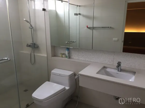 Condominium for rent in Sathon, Bangkok - Modern bathroom featuring a glass-enclosed shower, wide mirror cabinet, vanity and toilet with bidet hose.