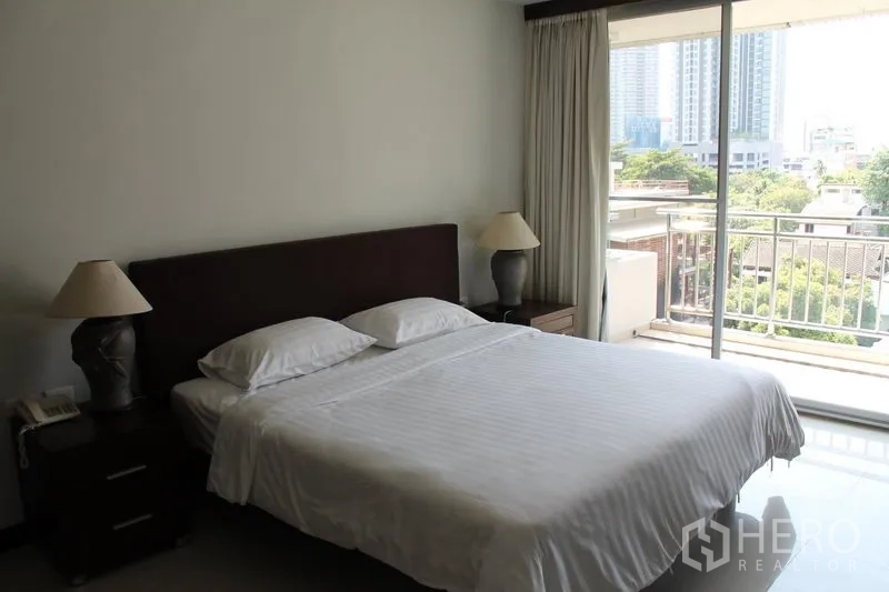 Apartment for rent in Bang Rak, Bangkok - Bright bedroom with sliding glass door to balcony overlooking greenery and towers.