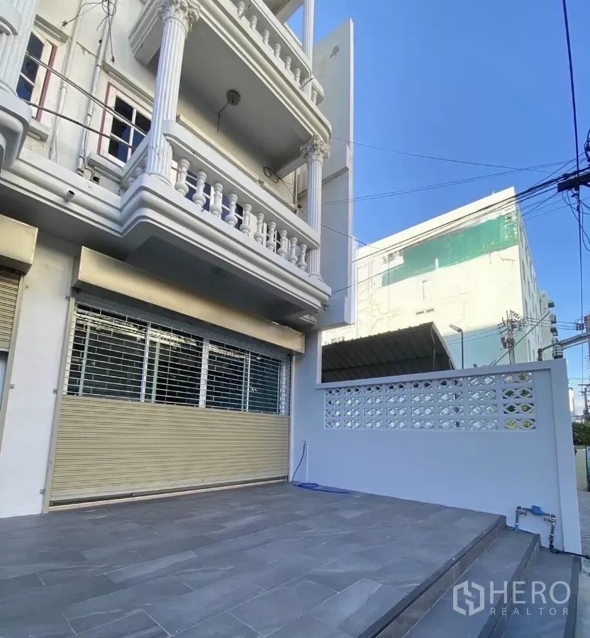 Townhouse for rent in Huai Khwang, Bangkok - Three-storey townhouse facade with classical columns and a tiled front terrace parking area in Huai Khwang, Bangkok.