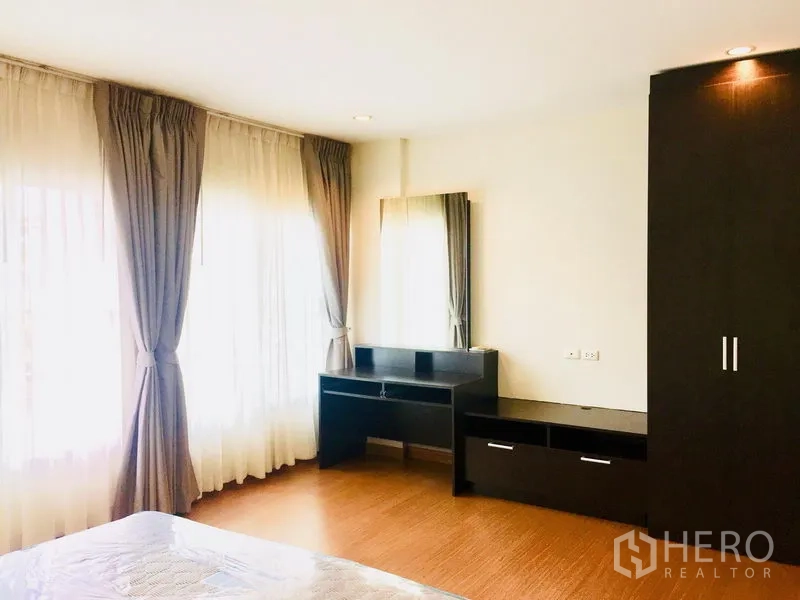 联排别墅 出租在Prawet, Bangkok - 宽敞卧室，转角窗采光，深色柜体与梳妆台。