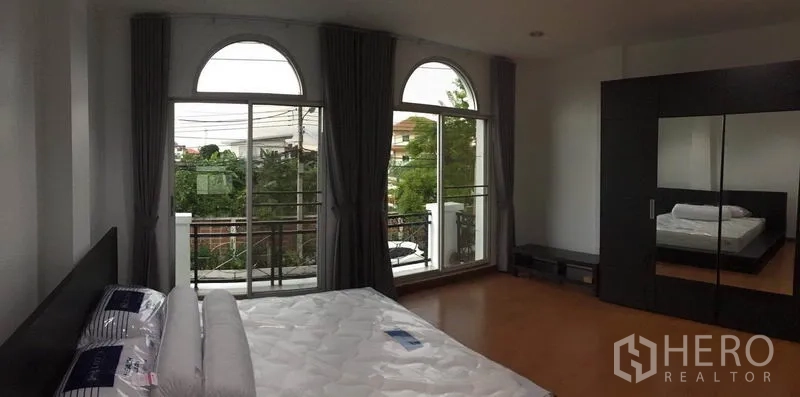 Townhouse for rent in Lat Phrao, Bangkok - Bedroom view to a balcony with twin arched windows and leafy outlook.