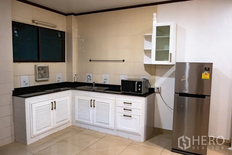 Home Office for rent in Khlong Toei, Bangkok - L-shaped white kitchen with black countertops, fridge and microwave.