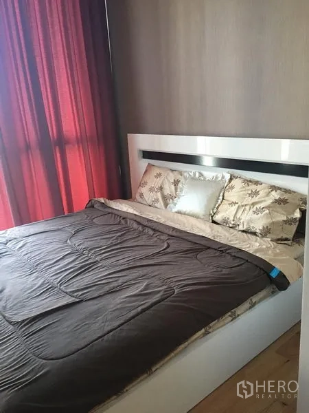 Condominium for rent or sale in Watthana, Bangkok - Cozy bedroom with double bed, patterned pillows and deep red curtains.