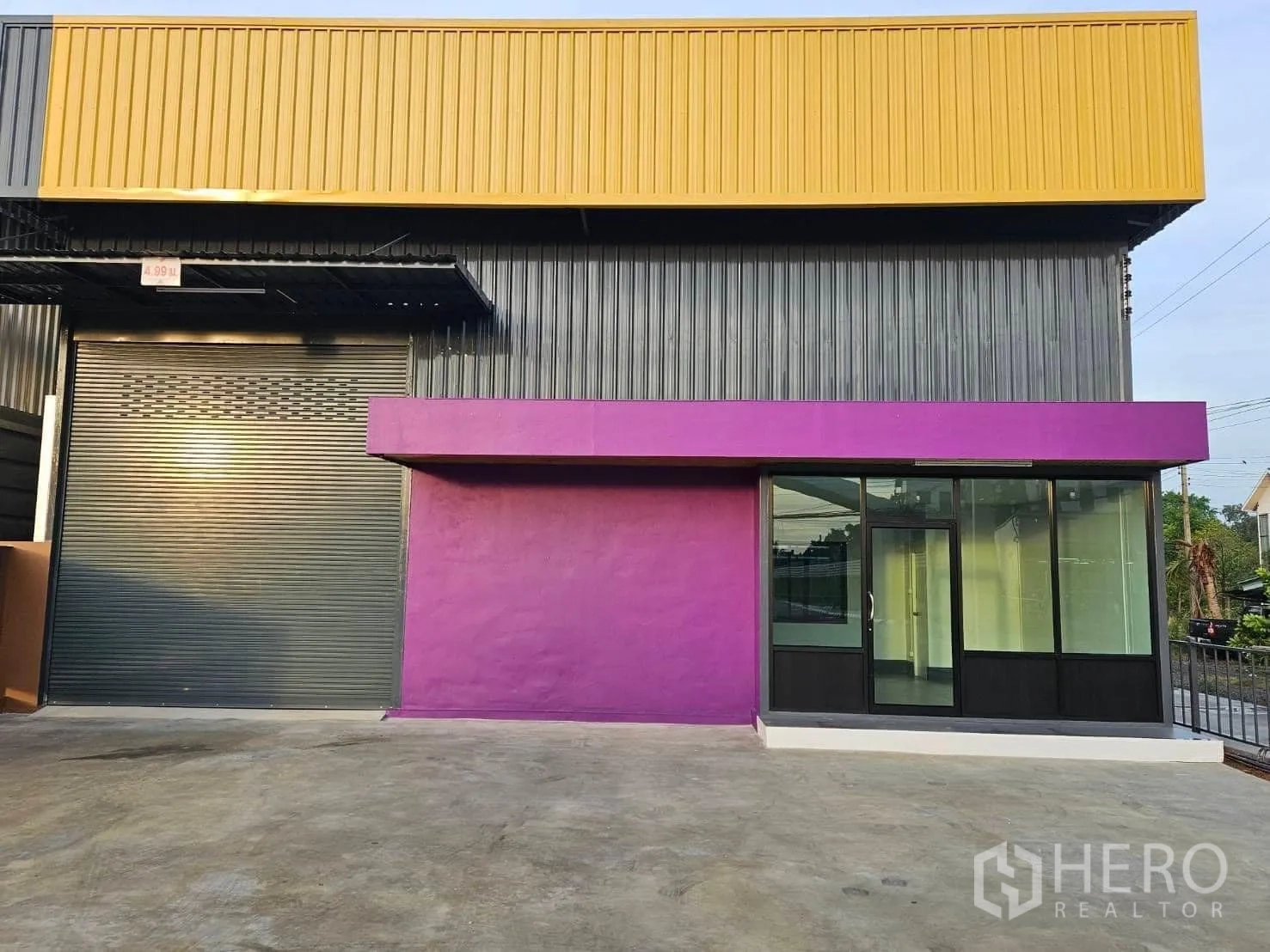 货栈 出租在Lam Luk Ka, Pathum Thani - 正立面近景，大型卷闸门与落地玻璃办公室窗并列。