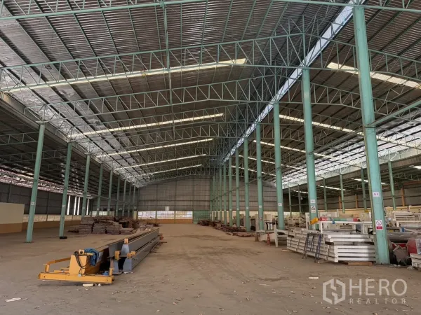 Factory for rent in Bang Na, Bangkok - Open production hall showing steel truss structure, stacked materials, and wide column bays.