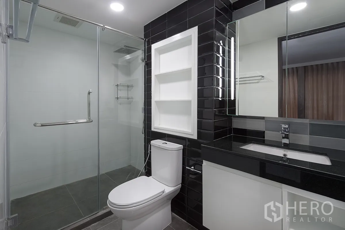 Condominium for rent in Khlong Toei, Bangkok - Modern bathroom with glass-enclosed rain shower, black subway tiles, and a sleek vanity.