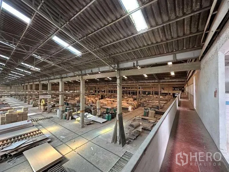 Factory for rent in Sai Noi, Nonthaburi - Elevated view of a spacious production hall with high metal roof, skylights, multi-bay columns and machinery.