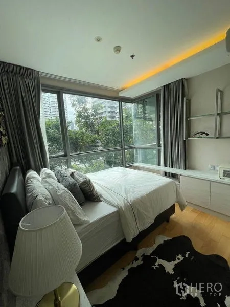 Condominium for rent in Watthana, Bangkok - Corner bedroom with wide windows on two sides, built-in shelving, and green city views.