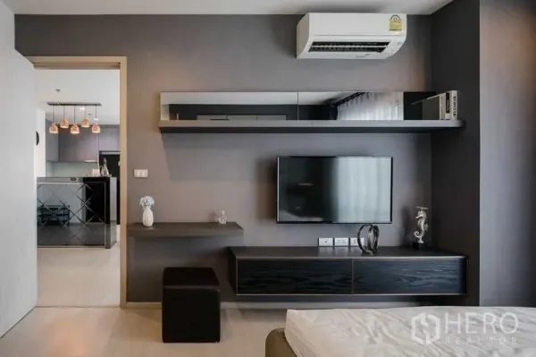 Condominium for rent in Khlong Toei, Bangkok - Bedroom media wall with shelves and TV, with a view toward the kitchen and pendant lights.