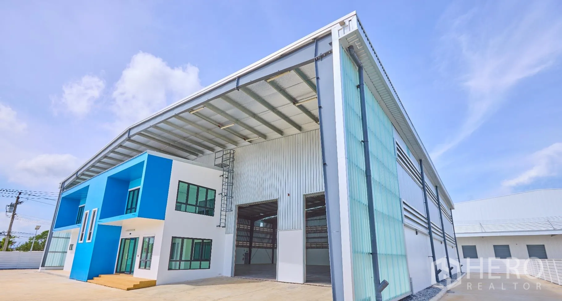 Factory for rent in Bang Sao Thong, Samut Prakan - Modern blue-and-white factory exterior with twin high electric roller shutters and a wide concrete yard.
