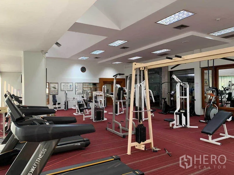 Condominium for rent or sale in Watthana, Bangkok - Fitness room equipped with treadmills, weight machines, and mirrors in a bright space.
