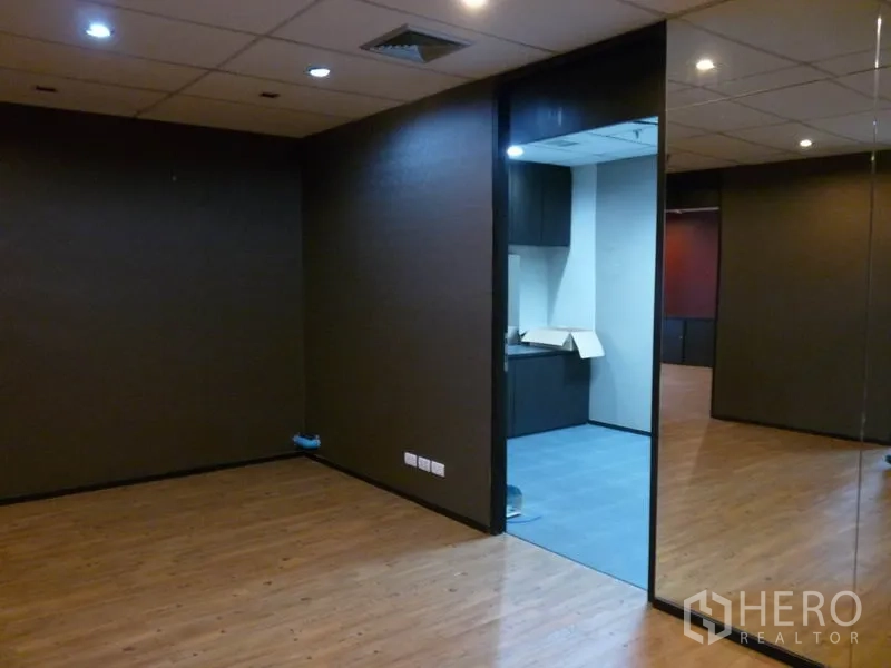 Office Space for sale in Watthana, Bangkok - Fitted office room with wood flooring, dark walls, recessed ceiling lights and a glass partition leading to a pantry area.
