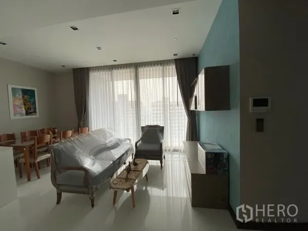Condominium for rent in Khlong Toei, Bangkok - Open living and dining area with sofa set and full-height curtains overlooking the Bangkok skyline.