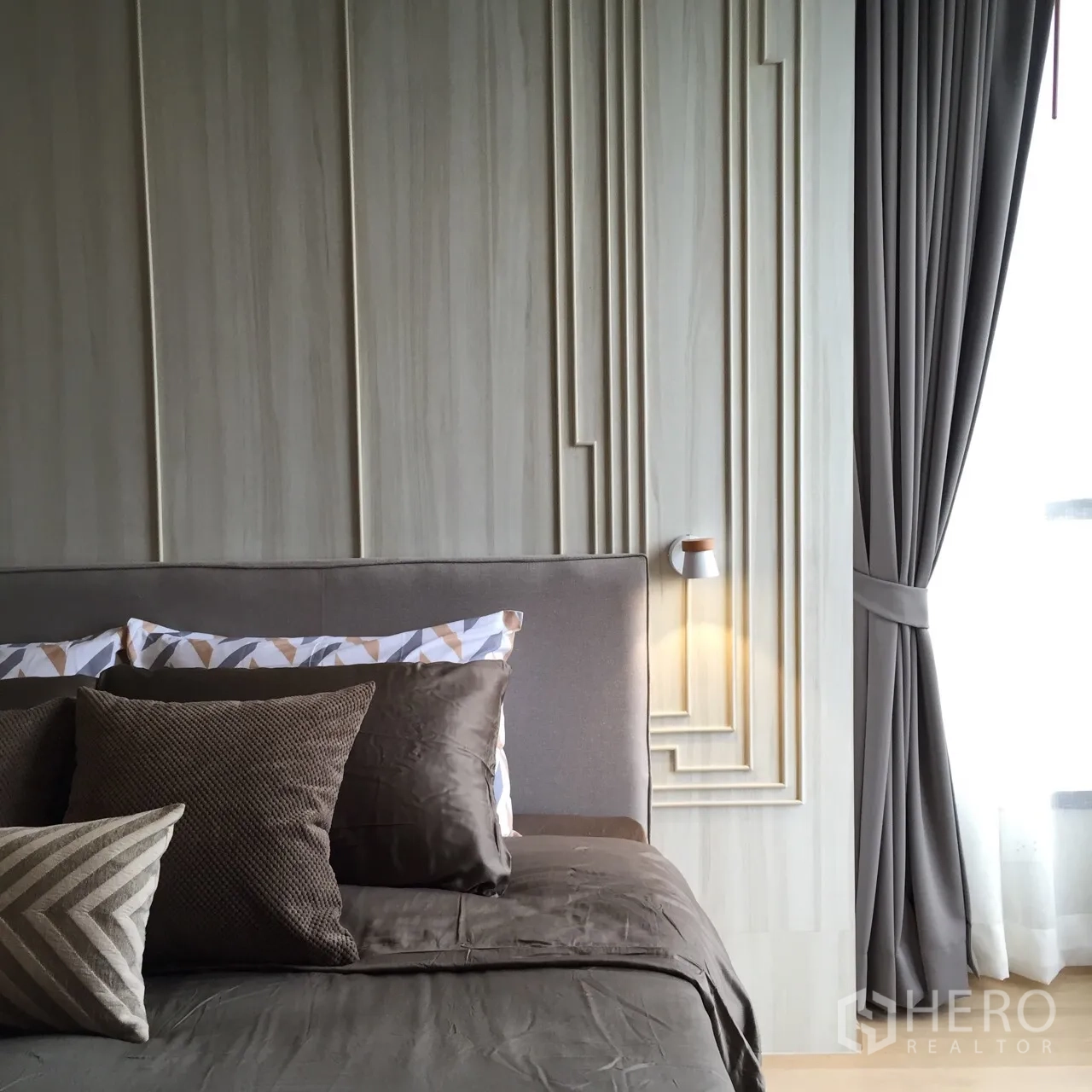 คอนโด ให้เช่าหรือขายในWatthana, Bangkok - ห้องนอนมาสเตอร์อบอุ่น ผนังแพเนล เตียงผ้าปูโทนน้ำตาล โคมไฟข้างเตียง และผ้าม่านโปร่ง